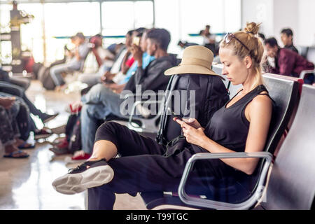 Female traveler talking on cell phone while waiting to board a plane at departure gates at asian airport terminal. Stock Photo