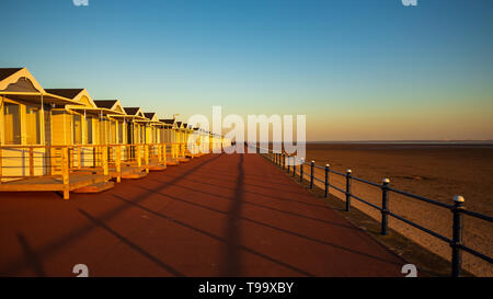 the early evening sunshine onto the ironwork seafront railings casts a long shadow along the centre of the prom in front of the st annes beach huts Stock Photo