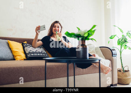 Happy young woman relaxing in living room and drinking smoothie. Healthy diet Stock Photo