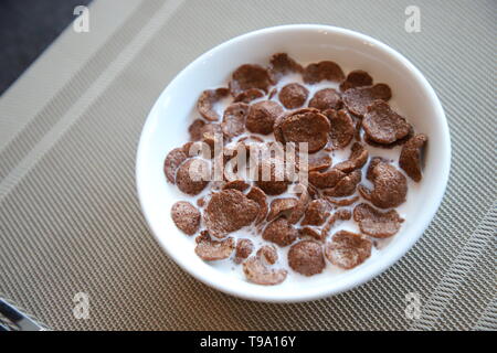 Breakfast Chocolate Cornflakes Cereal with milk in white bowl on the table Stock Photo