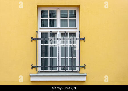 Window with a white rectangular frame and binding, located on the yellow wall of the house and closed decorative iron bars. From the series - Windows  Stock Photo