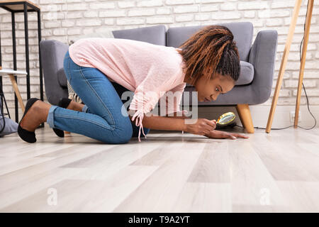 Side View Of A Young Woman Looking At Hardwood Floor Through Magnifying Glass Stock Photo