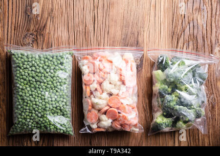 Set With Frozen Vegetables In Plastic Bags Over Wooden Desk Stock Photo