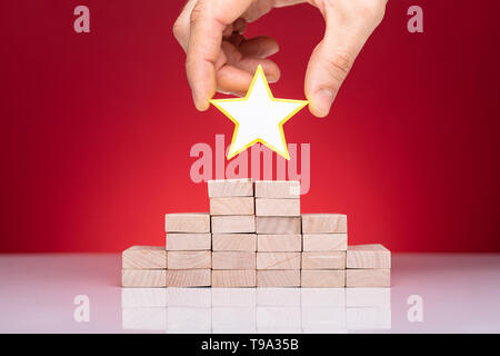 Close-up Of A Person's Hand Placing Yellow Star On Top Of Stacked Wooden Blocks Stock Photo