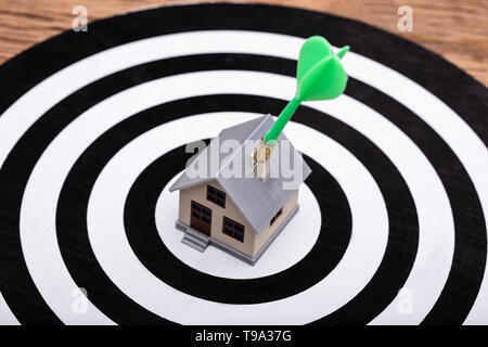 Close-up Of Green Dart Arrow Hitting House Model On Dartboard Stock Photo