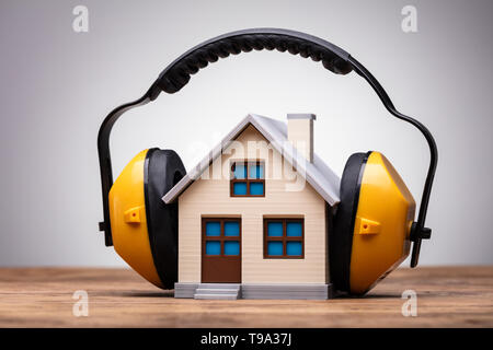Close-up Of Working Yellow Protective Headphone On The House Model Over The Wooden Table Stock Photo
