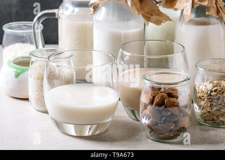 Variety of non-dairy vegan lactose free nuts and grain milk almond, hazelnut, coconut, rice, oat in glass bottles with ingredients above on white tabl Stock Photo