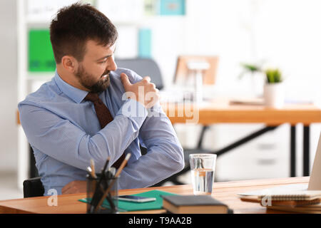 Businessman suffering from pain in shoulder at workplace Stock Photo