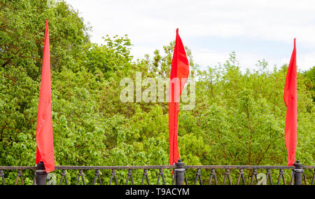 Three red colored flags fluttering or waving in the wind on the bridge at natural background. Festive decoration of the bridge Stock Photo