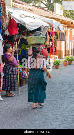 Indigenous Guatemalan woman in traditional clothing, walking on a cobblestone street, with a basket on her head in Panajachel, Guatemala Stock Photo