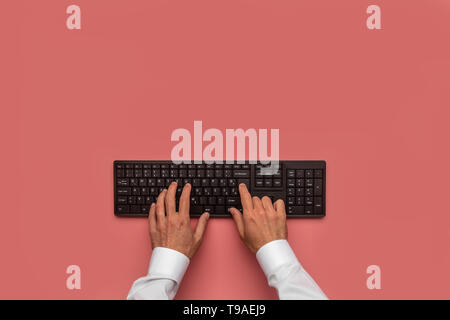 Top view of male hands typing on black computer keyboard. Over pink background. Stock Photo