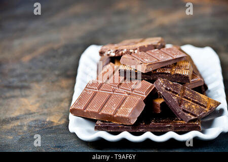 Chocolate bars pieces heap witn cinnamon powder on white ceramic plate. Sweet food photo concept. The chunks of broken chocolate stacked on black back Stock Photo