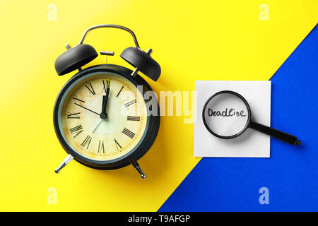 Alarm clock, magnifying glass and paper with word DEADLINE on color background Stock Photo