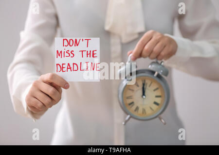 Woman holding alarm clock and paper sheet with text DON'T MISS THE DEADLINE, closeup Stock Photo
