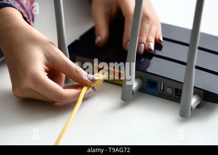 Woman inserting ethernet wire into wi-fi router on table in room Stock ...