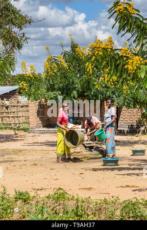 Malawian women drawing water in midday sun from a shallow well in a village using plastic buckets and rope Stock Photo