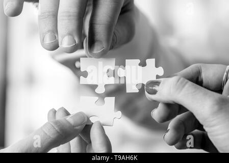 Black and white image of three people, male and female, holding puzzle pieces to match them. Conceptual of teamwork, cooperation and problem solving. Stock Photo