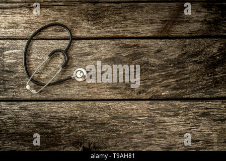 Top view of black medical stethoscope lying on aged textured wooden planks with additional copyspace to the right. Stock Photo
