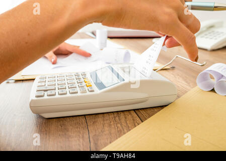 Bookkeeper doing calculations on an adding machine checking the totals against those in the journals, close up of her hands and the machine on a woode Stock Photo