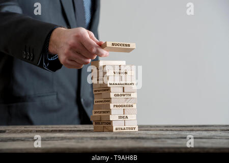 Businessman in black suite building tower of wooden domino bricks with motivational business concept signs about company building strategy. Close-up o Stock Photo