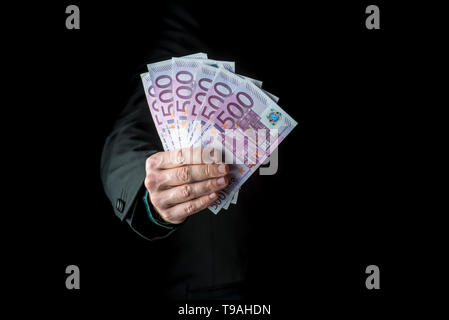 Businessman holding a fistful of 500 euro banknotes extended to the camera conceptual of wealth, success or payoff, cropped closeup over black backgro Stock Photo