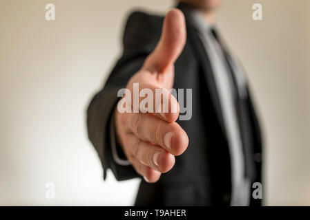 Close-up view of businessman hand reached out to handshake. Incognito man in suit blurred in background. Stock Photo