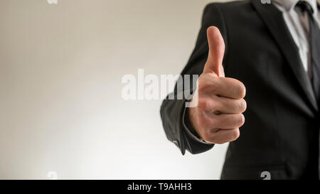 Close-up view of incognito businessman in black suit thumbs up gesture standing on light background with copy space. Stock Photo