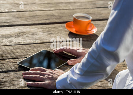 Closeup of businessman using digital tablet on rustic wooden desk with orange coffee mug next to him. Stock Photo