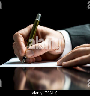 Businessman writing on a sheet of white paper with a fountain pen as he signs an agreement or contract, writes correspondence, takes notes or complete Stock Photo