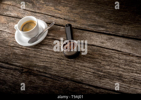 Cup of fresh hot Arabica black coffee and freshly ground coffee beans in the metal measure of a coffee machine lying on a textured rustic wooden board Stock Photo
