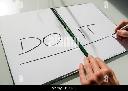 Do It concept with the hand of a man writing the words in large capital letters across an open notebook conceptual of - do not procrastinate, do it im Stock Photo