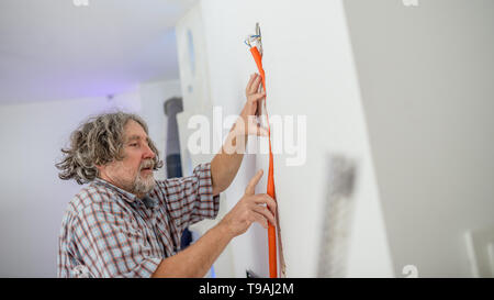 Electrician installing recessed wiring in a wall fitting the conduit into the groove , low angle view in a house renovation concept. Stock Photo
