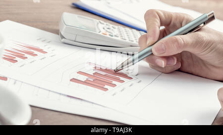 Closeup of female business accountant pointing to a graph with a pen as she works on tax report, with a retro filter effect. Stock Photo