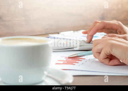 Hands of a businesswoman working on graphs analyzing the statistics using a desktop calculator, close up view. Stock Photo