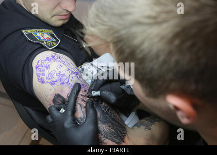 Kyiv, Ukraine. 17th May, 2019. Master tattoos a man dressed in police uniform during the tattoo festival in Kyiv, Ukraine, May 17, 2019. 15th international festival of tattoo ''International Tattoo Convention'' takes place in Kyiv. Credit: Sergii Kharchenko/ZUMA Wire/Alamy Live News Stock Photo