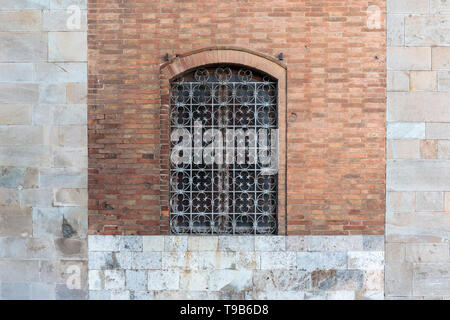 Rusty ornate window bars in a brick and stone wall in Pisa. Stock Photo