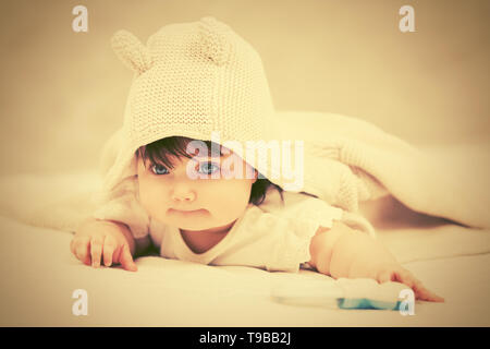 Baby girl in a hoodie sweatshirt crawling on blanket at home Stock Photo