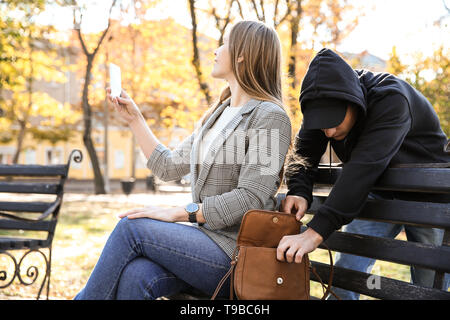 Male thief stealing bag from young carefree woman in park Stock Photo