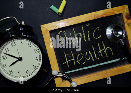 The words Public Health handwriting on chalkboard on top view. Alarm clock, stethoscope on black background. With education, medical and health concep Stock Photo