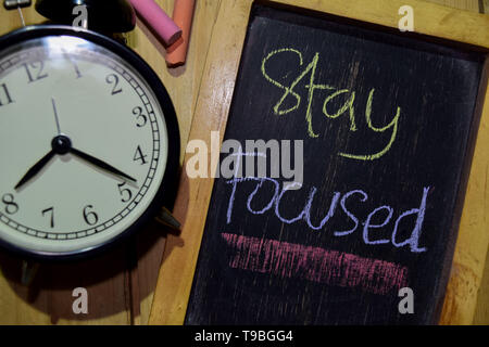 Stay Focused on phrase colorful handwritten on chalkboard and alarm clock with motivation, inspiration and education concepts. Table background Stock Photo
