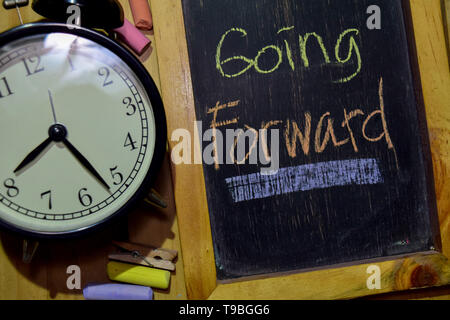 Going Forward on phrase colorful handwritten on chalkboard and alarm clock with motivation, inspiration and education concepts. Table background Stock Photo