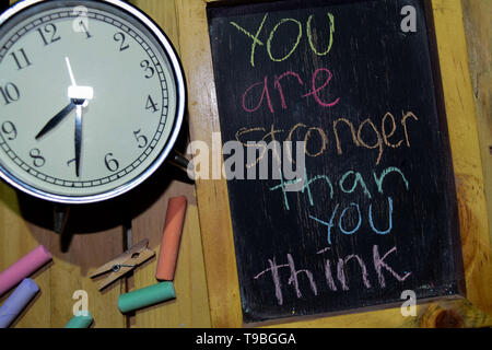 You Are Stronger Than You Think on phrase colorful handwritten on chalkboard and alarm clock with motivation, inspiration and education concepts. Tabl Stock Photo