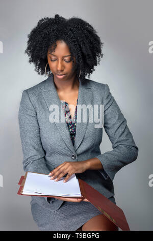 Black African American Businesswoman sitting and holding a folder of contracts or documents.  She looks like a secretary or a manager giving a busines Stock Photo