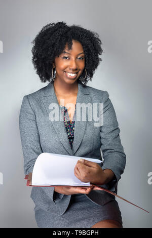 Black African American Businesswoman sitting and holding a folder of contracts or documents.  She looks like a secretary or a manager giving a busines Stock Photo