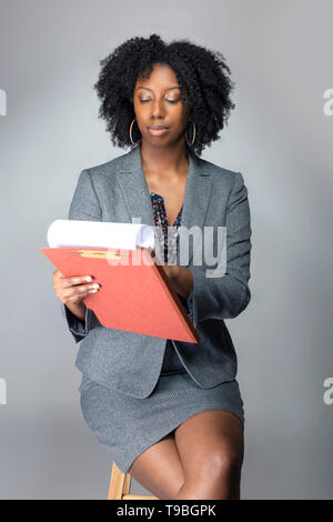 Black African American Businesswoman sitting and holding a folder of contracts or documents.  She looks like a secretary or a manager giving a busines Stock Photo