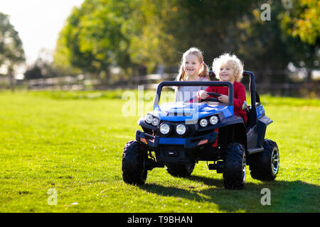 Kids driving electric toy car in summer park. Outdoor toys. Children in battery power vehicle. Little boy and girl riding toy truck in the garden. Fam Stock Photo