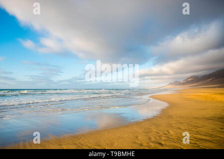 Summer solitary beach with water reflections concept - beautiful landscape with ocean and waves - blue sky and mountains in backgrund - coloured hevan Stock Photo
