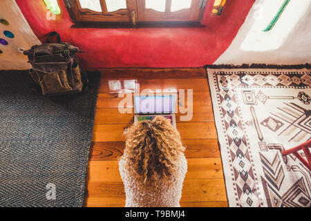 Above view of blonde curly hair beautiful woman lay down on the wooden floor working at computer laptop - hotel or home alternative office for job - s Stock Photo