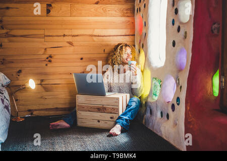 Alternative blonde middle age pretty woman sit down in artistic home and looking outside the window while have a break with tea or coffee and use comp Stock Photo