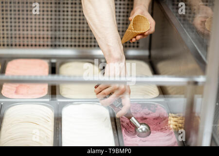 Man taking ice cream from the metal trays with scoop in the refrigerator at the shop, close-up view Stock Photo